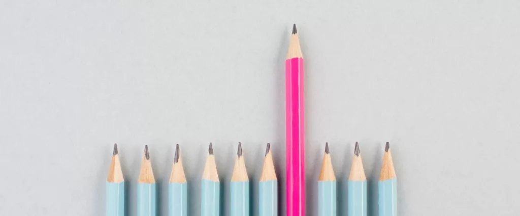 photo épurée montrant une série de crayons à papier bleu clair, sauf un qui est rose et qui se distingue par sa taille.